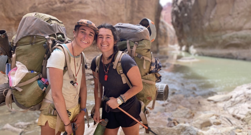 A group of gap year students wearing backpacks pose for a photo in front of water flowing through a canyon.